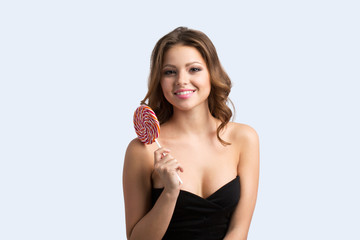 Happy woman with lollipop standing in elegant black dress isolated.