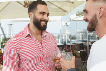 Handsome bearded man laughing, enjoying drinks with his friends on a summer party