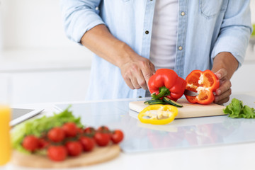 Obraz na płótnie Canvas Close up of male hand cutting pepper on cutting board at home.