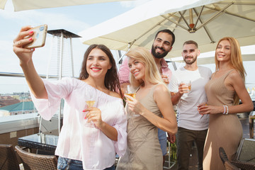 Group of friends taking selfies on a smart phone together during rooftop party