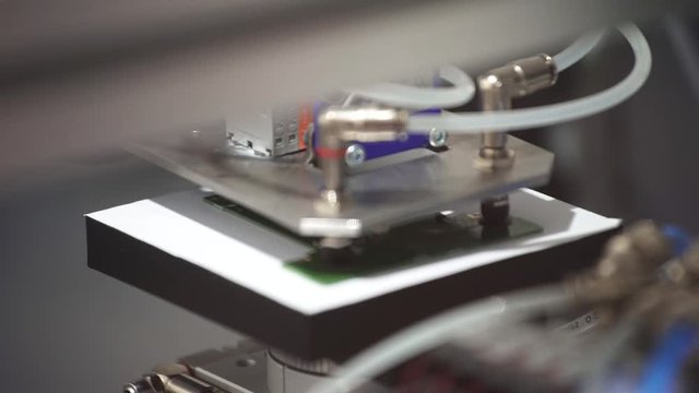 The robot hand takes the pcb from the test equipment and puts it on conveyor. Automation machine equipment for quality testing of printed circuit boards - close up