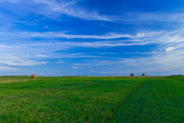 picturesque horizon landscape scenic view of agriculture rural field with stack of hay on green grass end of summer season in August month, clear weather evening