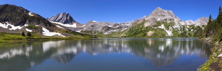 Fototapeta na wymiar Wide Panoramic Landscape View of Scenic Aster Lake, Green Alpine Meadow and Rugged Rocky Mountain Peaks on a hiking trail in Kananaskis Country, Alberta, Canada on a sunny summertime day 