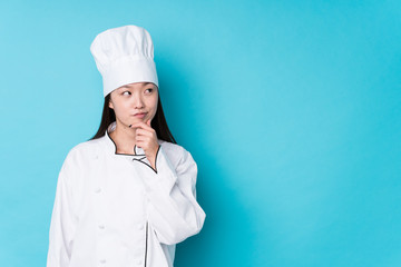 Young chinese chef woman isolated looking sideways with doubtful and skeptical expression.
