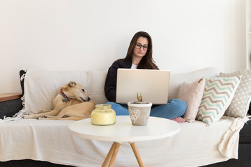 Young woman with a laptop doing home working in companion of her dog.