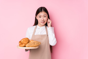 Young chinese baker woman isolated covering ears with hands.