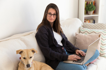 Young woman with a laptop doing home working in companion of her dog.
