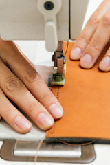 close up of hands sewing a piece of leather on a sewing machine