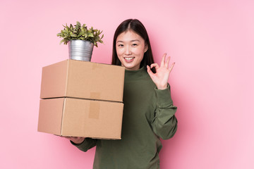 Young chinese woman holding boxes isolated cheerful and confident showing ok gesture.