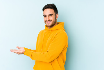 Young caucasian man isolated on blue background holding a copy space on a palm.