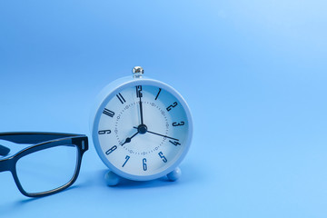 Alarm clock and eyeglasses on blue background 