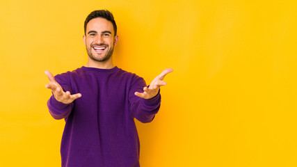 Young caucasian man isolated on yellow bakground feels confident giving a hug to the camera.