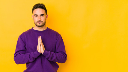 Young caucasian man isolated on yellow bakground praying, showing devotion, religious person...