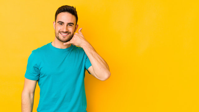 Young caucasian man isolated on yellow bakground showing a mobile phone call gesture with fingers.