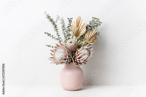 Beautiful dried flower arrangement in a stylish pink vase. In the flower bunch is pink King Proteas, Banksia, Eucalyptus leaves and golden Palm fronds, photographed on a white background.