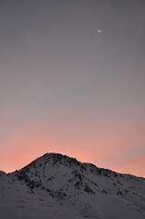 winter sunset over snowy mountain and the moon in the background
