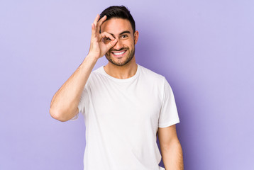Young caucasian man isolated on purple background excited keeping ok gesture on eye.