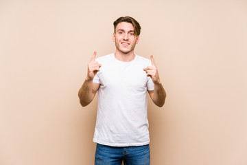 Young caucasian man posing isolated indicates with both fore fingers up showing a blank space.
