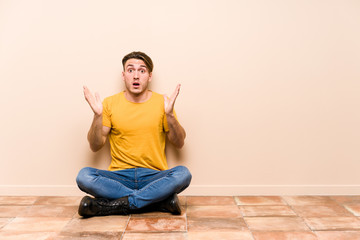 Young caucasian man sitting on the floor isolated surprised and shocked.