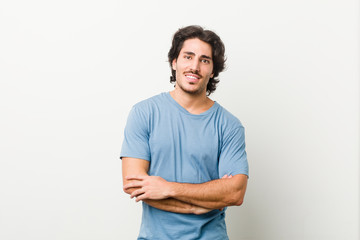 Young handsome man against a white background who feels confident, crossing arms with determination.