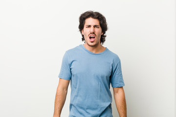 Young handsome man against a white background screaming very angry and aggressive.