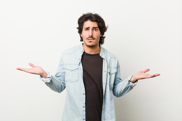 Young handsome man against a white background confused and doubtful shrugging shoulders to hold a...