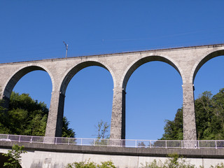 Fototapeta na wymiar gigantic impressive railway viaduct without train in front of blue sky and green forest with a highway and guardrails by day without people