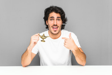 Young man holding a magic lamp surprised pointing at himself, smiling broadly.