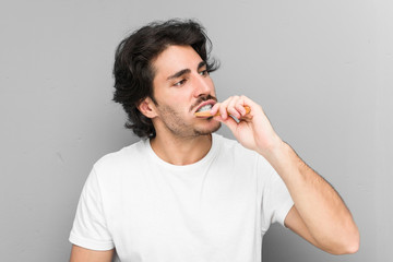 Young caucasian man cleaning his teeth with a toothbrush isolated in a grey background
