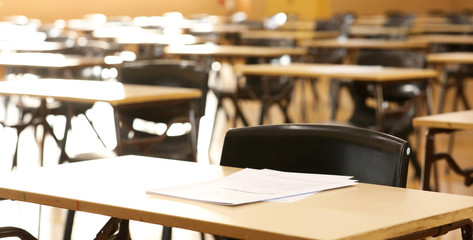 A large high school hall or room set up ready for an end of year final exam to be sat by students. examination paper sitting on the edge of a desk or table.