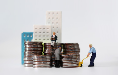 A building and a pile of coins. A miniature people on a pile of coins and a miniature man carrying...