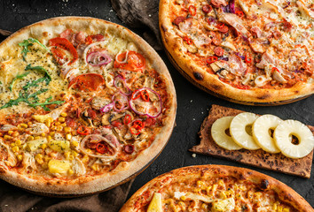 Variety of pizzas with meat, sausage, ham, prosciutto, salami, chicken fillet, pepperoni, cheese, greens, vegetables on wooden board on black background. Fast food lunch for picnic company, top view