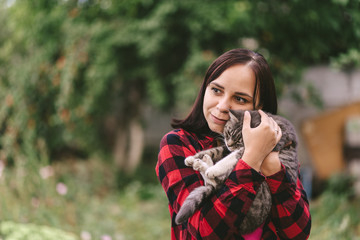 Close up of young woman holds domestic cat in hands. Brunette strokes cute pussycat on street in...