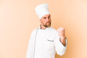 Chef man isolated on beige background showing fist to camera, aggressive facial expression.