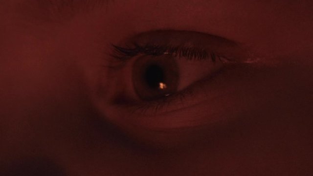 Static close up FHD shot of a human eye looking into a fire and slowly closing and falling asleep in the evening filled with a flickering firelight. Closing human eye slowly falling asleep.