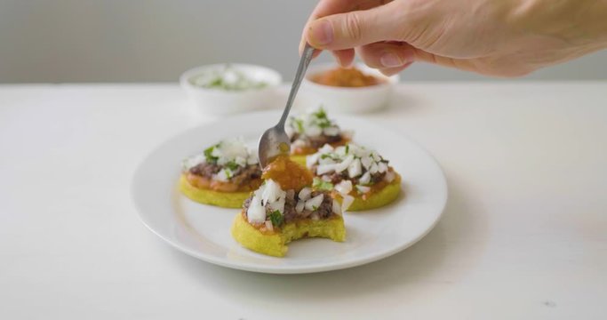 Man's Hand Puts Tomato Sauce and Raw Onion on a "Sope" also known as "Picadita", Traditional Mexican Dish on a White Background