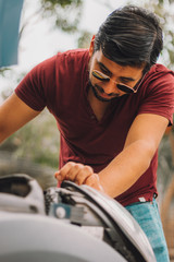 Joven adulto mexicano latino arregla auto en la calle en dia soleado