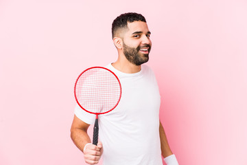 Young arabian man playing badminton isolated looks aside smiling, cheerful and pleasant.