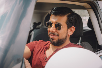 Joven adulto mexicano latino conduce su auto en día soleado en vacaciones en Mexico con lentes...