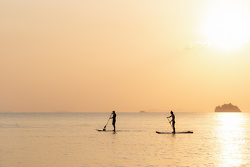 Couple swims on paddle boards on the sea against the backdrop of islands and golden sunset