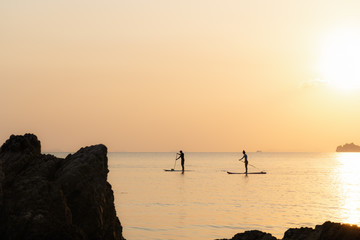 Couple swims on paddle boards on the sea against the backdrop of islands and golden sunset