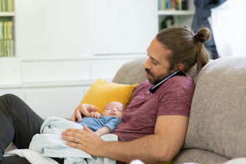 Caucasian man father talking on mobile phone for online cooperate working with holding his sleeping newborn baby son. Single dad caring his infant child boy. Happy family and working at home concept.