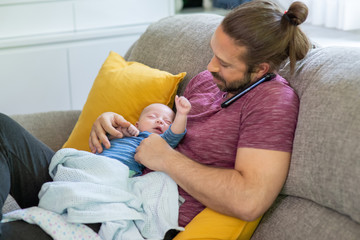 Caucasian man father talking on mobile phone for online cooperate working with holding his sleeping newborn baby son. Single dad caring his infant child boy. Happy family and working at home concept.
