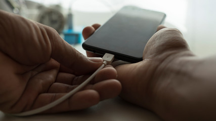 Hand of a man charging his cell phone, warm tones.