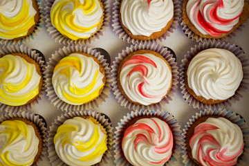 Boxed cupcakes, cupcake packaging, cupcakes with yellow, red and white cream. Set of different delicious homemade cupcakes in cardboard stand. Top view.