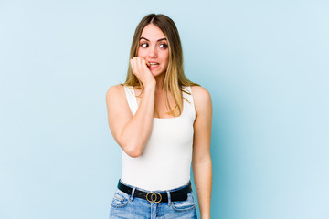 Young caucasian woman isolated on blue background biting fingernails, nervous and very anxious.