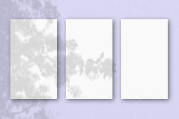 3 vertical sheets of textured white paper on lilac table background. Mockup overlay with the plant shadows. Natural light casts shadows from an exotic plant. Horizontal orientation