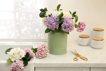 Bouquet with beautiful hydrangea flowers in can and scissors on light countertop