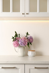 Bouquet with beautiful purple hydrangea flowers and jar on light countertop