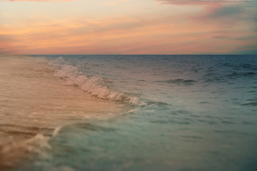 Fototapety  Fale oceanu toczące się po piaszczystej plaży pod niebem z chmurami o zachodzie słońca, zbliżenie